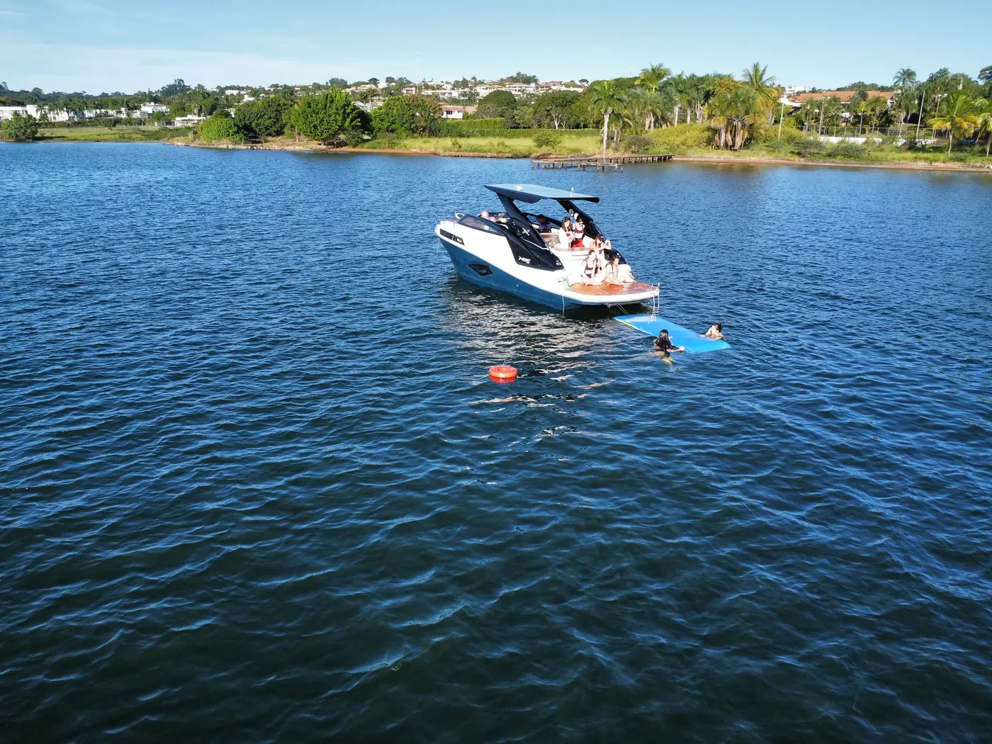Lancha ancorada no Lago Paranoá com boia e pessoas tomando banho de lago